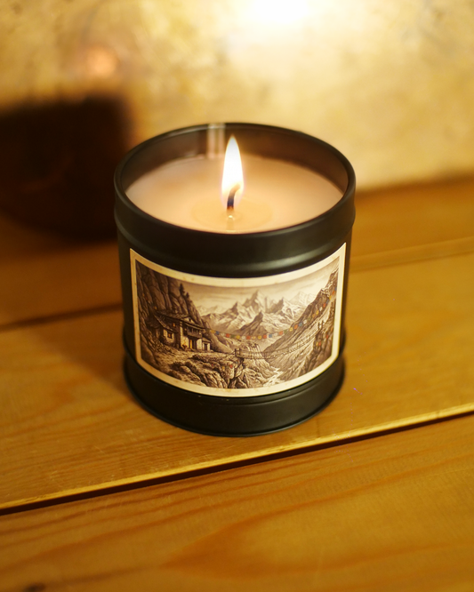 Himalayan Teahouse candle burning, warm flame above an etched label of snow-capped peaks and strung prayer flags — Wayward