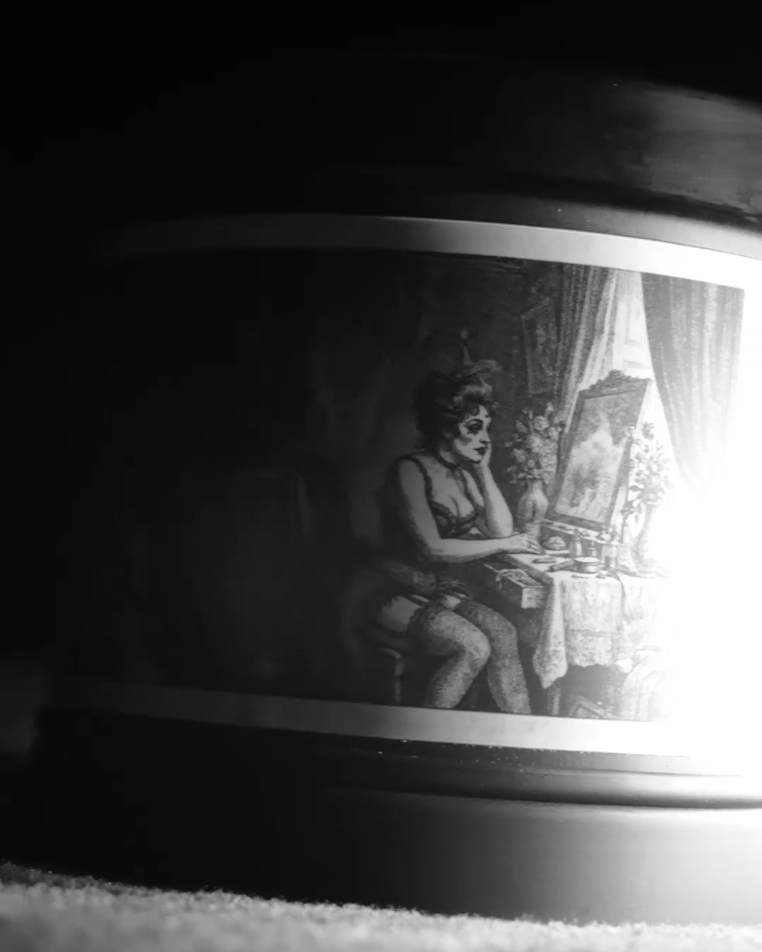 Black-and-white advert still: a shaft of light falls across the Parisian Boudoir tin, catching the etched dressing-room label
