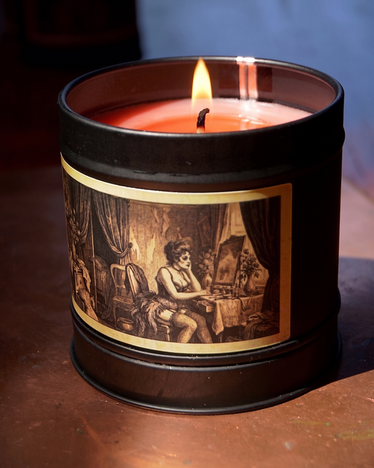 risian Boudoir candle burning with deep red wax, close on the etched label of a dressing room — heavy drapes, a vanity mirror, a woman at her table — Wayward