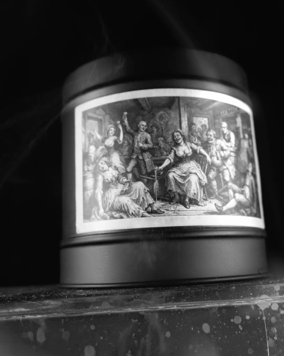 Black-and-white advert still: the Victorian Gin House tin with a thread of smoke rising, etched tavern label in full light